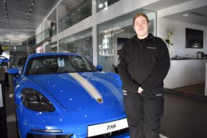 Former student standing in front of a Porsche at the showroom.