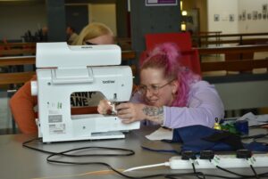 Artist and volunteer sat at sewing machine