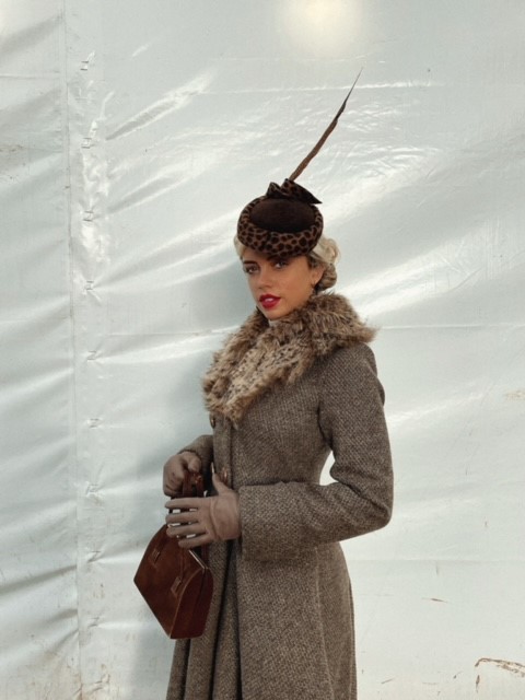 Grace behind the scenes in a coat and feather hat
