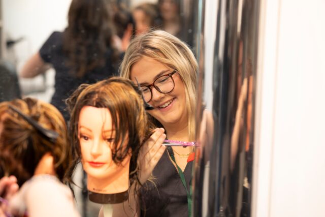 a doll head with someone working behind it doing its hair