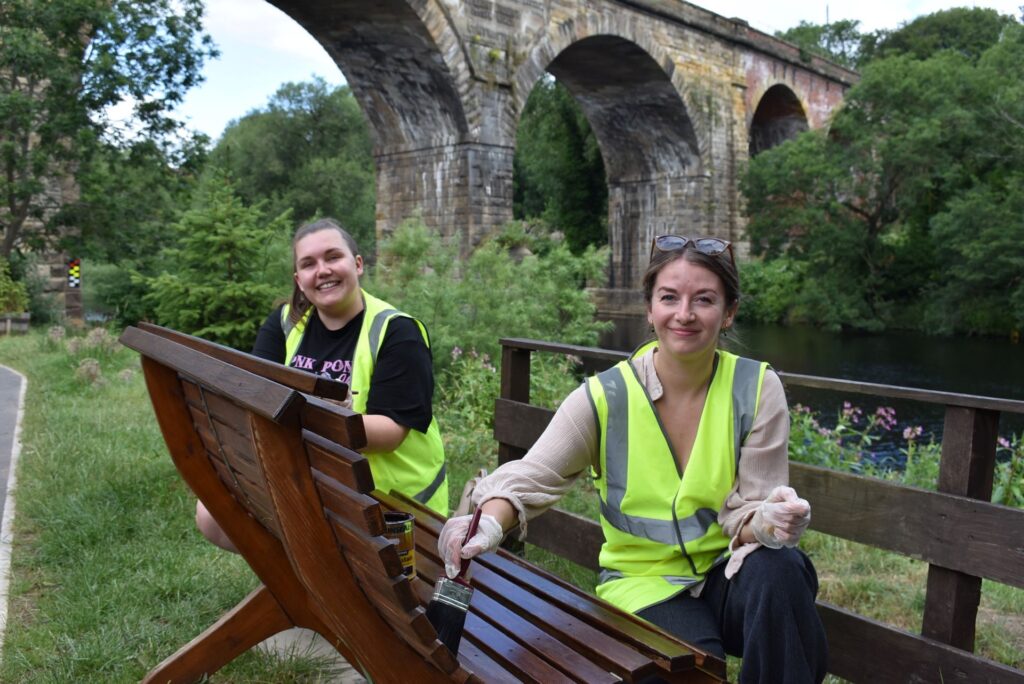 Two Etc. staff sanding a bench by the riverside in Yarm.