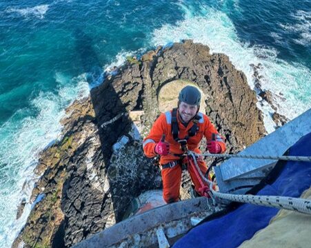 someone on a rope in orange high vis on a cliff edge with the sea below them