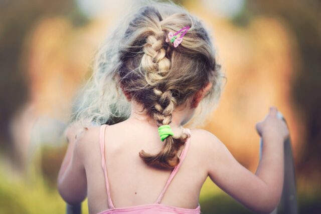 back of a child's head with multicoloured bobbles holding a long plait in place