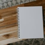 a white notebook with a black ringbinder spine sits on a wooden table. There is nothing on the page.